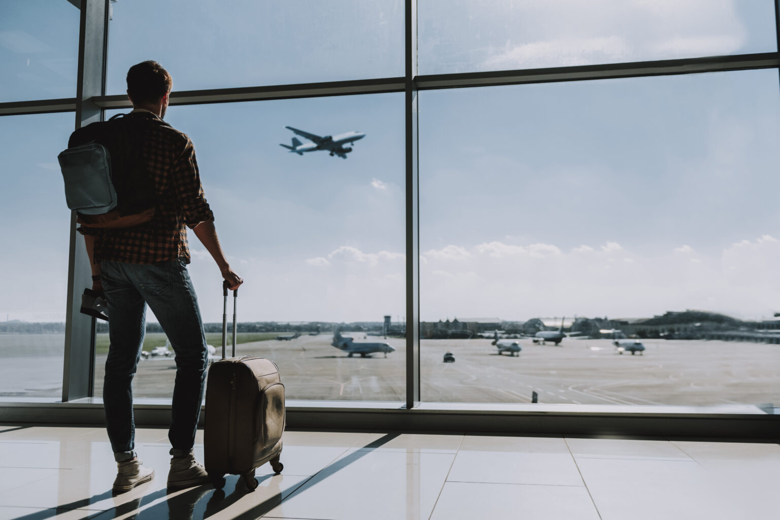 Un uomo pronto per viaggiare guarda gli aerei partire dall'interno di un aeroporto